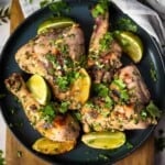 Cooked chicken pieces on a round blue plate sitting on top of a brown cutting board.