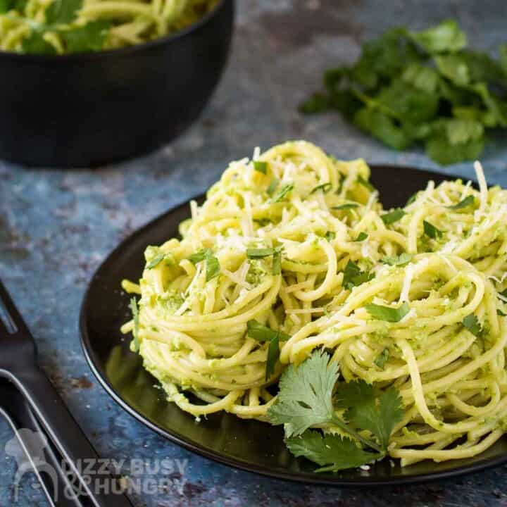 Side shot of green spaghetti garnished with parmesan and parsley leaves on a black plate.