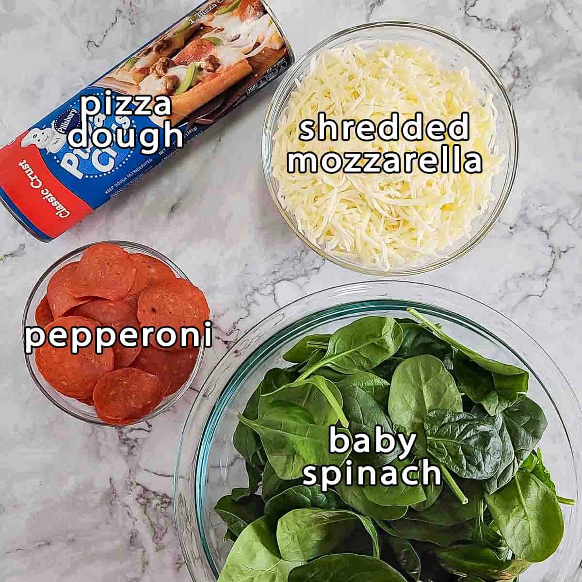 Overhead shot of ingredients - pizza dough, shredded mozzarella, pepperoni, and baby spinach.
