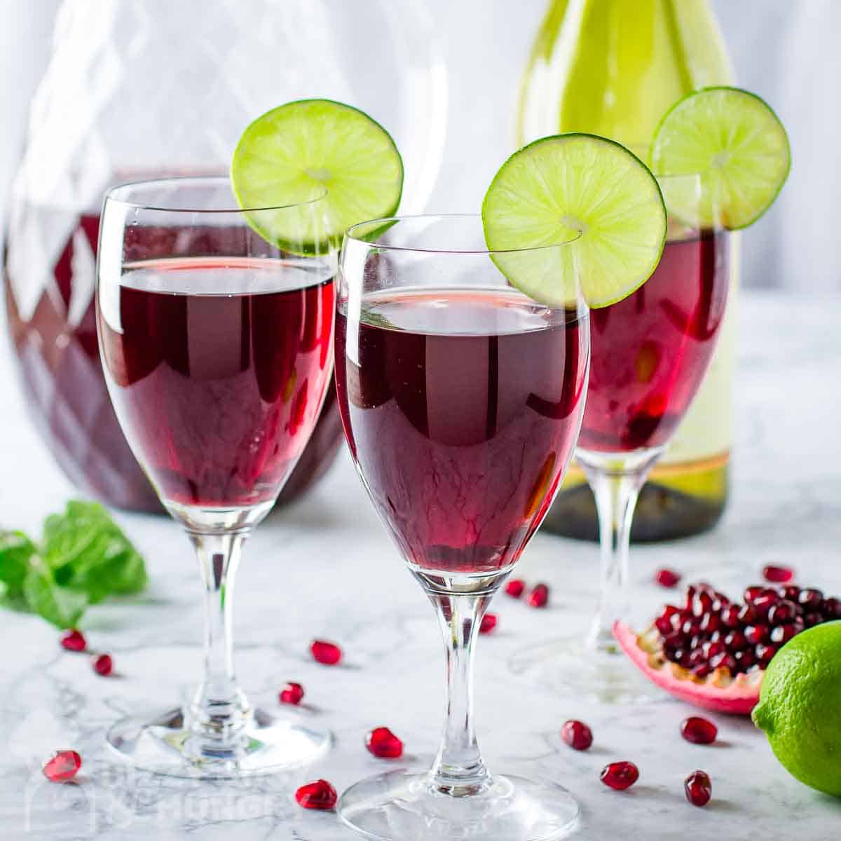 Side shot of three wine glasses with pomegranate cocktail with a lime wedge on the rim.
