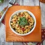 Overhead shot of mexican mac and cheese garnished with cilantro in a white bowl on orange and red cloths with a fork on the side.