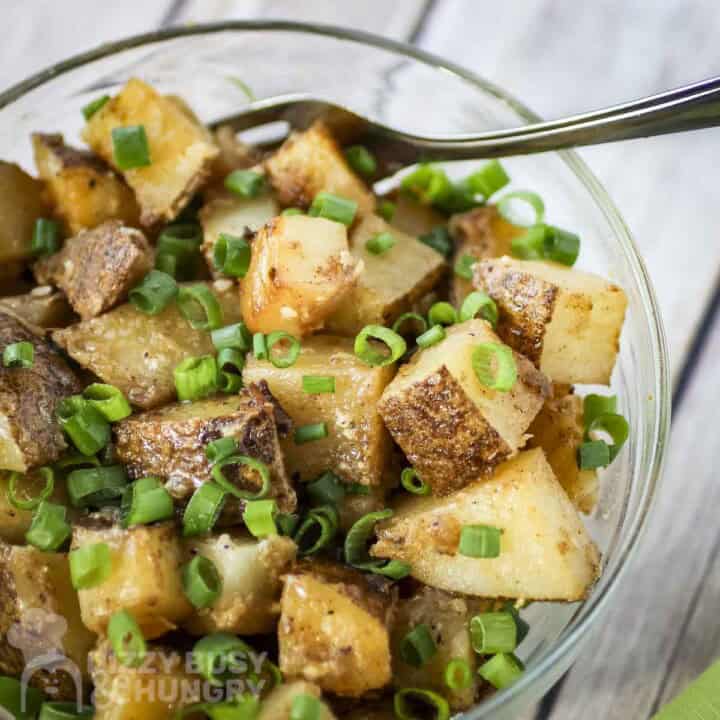 Overhead shot of chipotle potatoes in a clear bowl with a fork on the side and garnished with green onions.