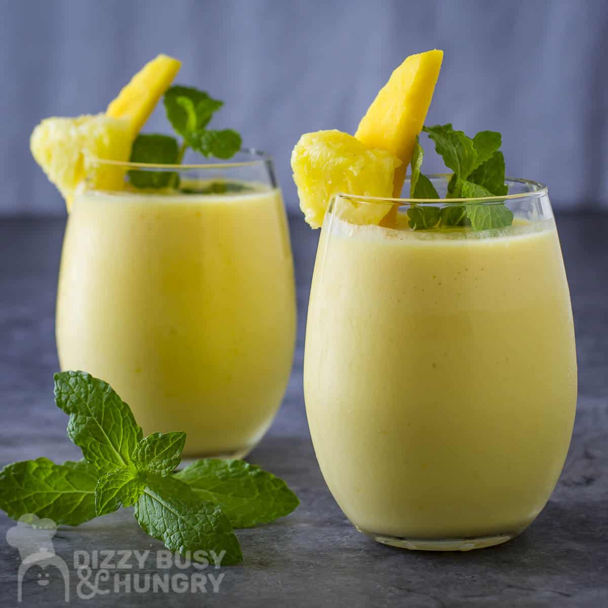 Side shot of two cocktail glasses with pineapple smoothie garnished with mango and mint.