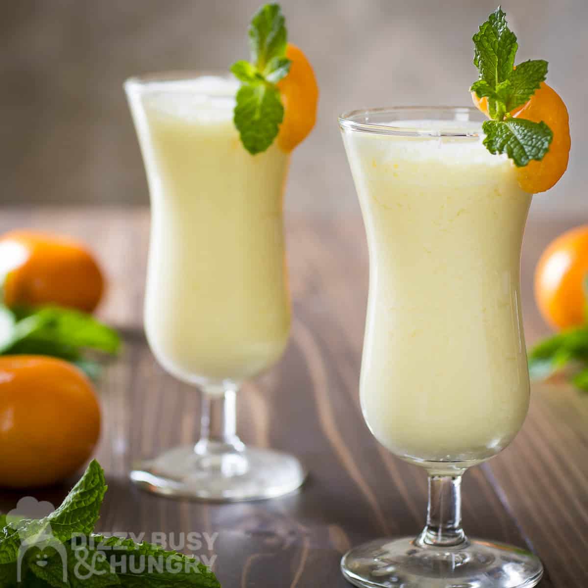 Side shot of two cocktail glasses with orange pineapple smoothie garnished with orange slices.