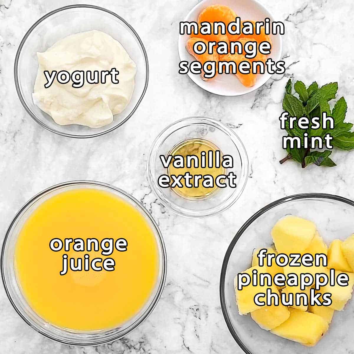 Overhead shot of ingredients - mandarin orange segments, yogurt, vanilla extract, fresh mint, orange juice, and frozen pineapple chunks.