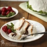 Side shot of a slice of angel food cake in a white bowl with raspberries, mint, and a fork on the side.