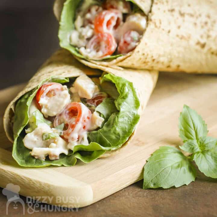 Side close up shot of blue cheese chicken wraps on a wooden cutting board with basil on the side.