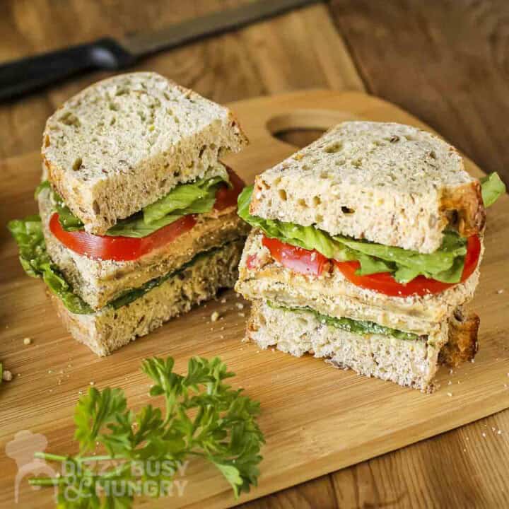 Side shot of a milanese sandwich cut in half on a wooden cutting board with fresh herbs on the side.