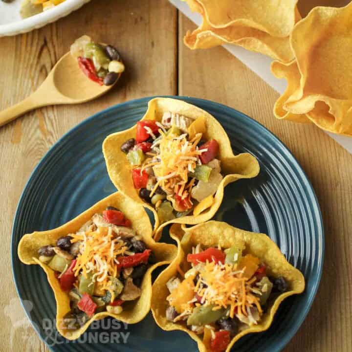 Overhead shot of three tortilla bowls on a blue plate with a spoon and more empty tortilla bowls on the side.