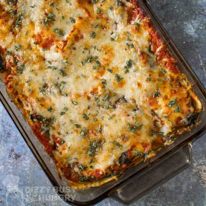 Overhead shot of ravioli bake garnished with fresh herbs in a casserole dish on a blue marble surface.