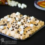 Side shot of monster mash sprinkled with chocolate chips and mini marshmallows on a black plate with more marshmallows in the background.