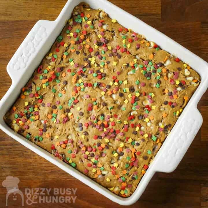 Overhead shot of spice cake with fall-themed sprinkles in a white square baking dish on a wooden surface.