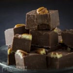 Side shot of multiple pieces of fudge stacked on each other on a clear plate with a black background.