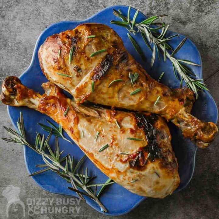 Overhead view of two turkey legs garnished with rosemary on a blue decorative plate with rosemary sprigs on the side.