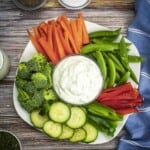 Overhead shot of a white platter with veggies surrounding a clear bowl with homemade ranch dressing.