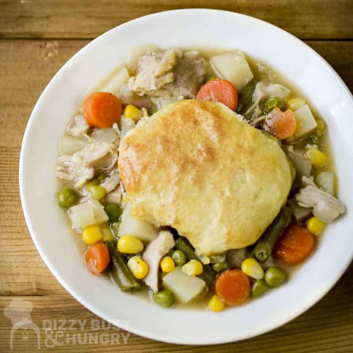 Overhead shot of chicken and biscuits on a white plate on a wooden surface.