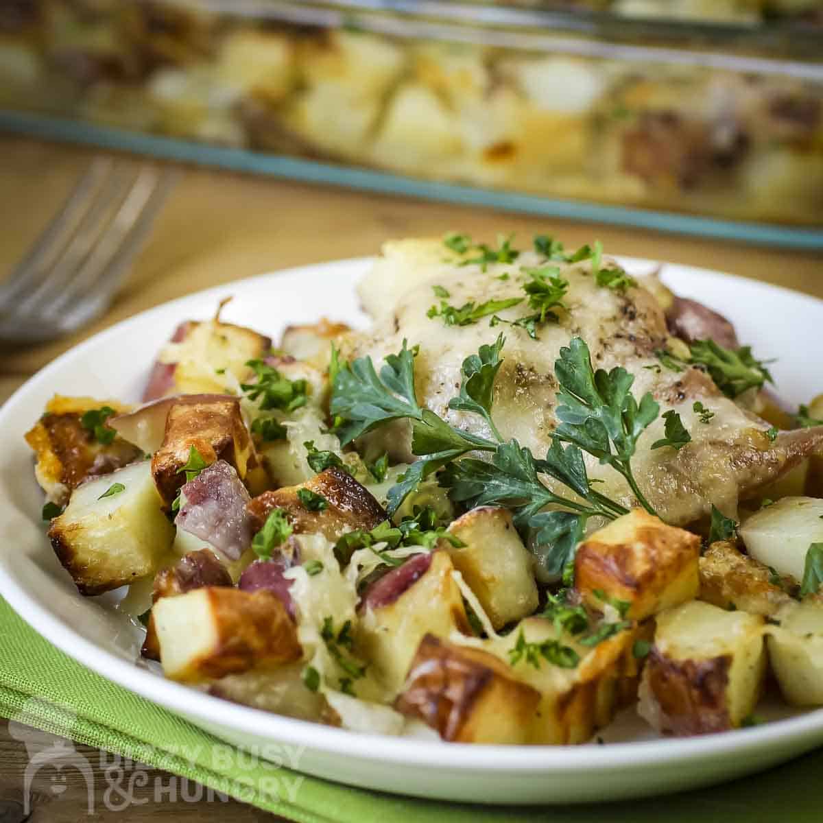 Close up shot of potato chicken bake on a white plate garnished with fresh herbs on a green cloth.