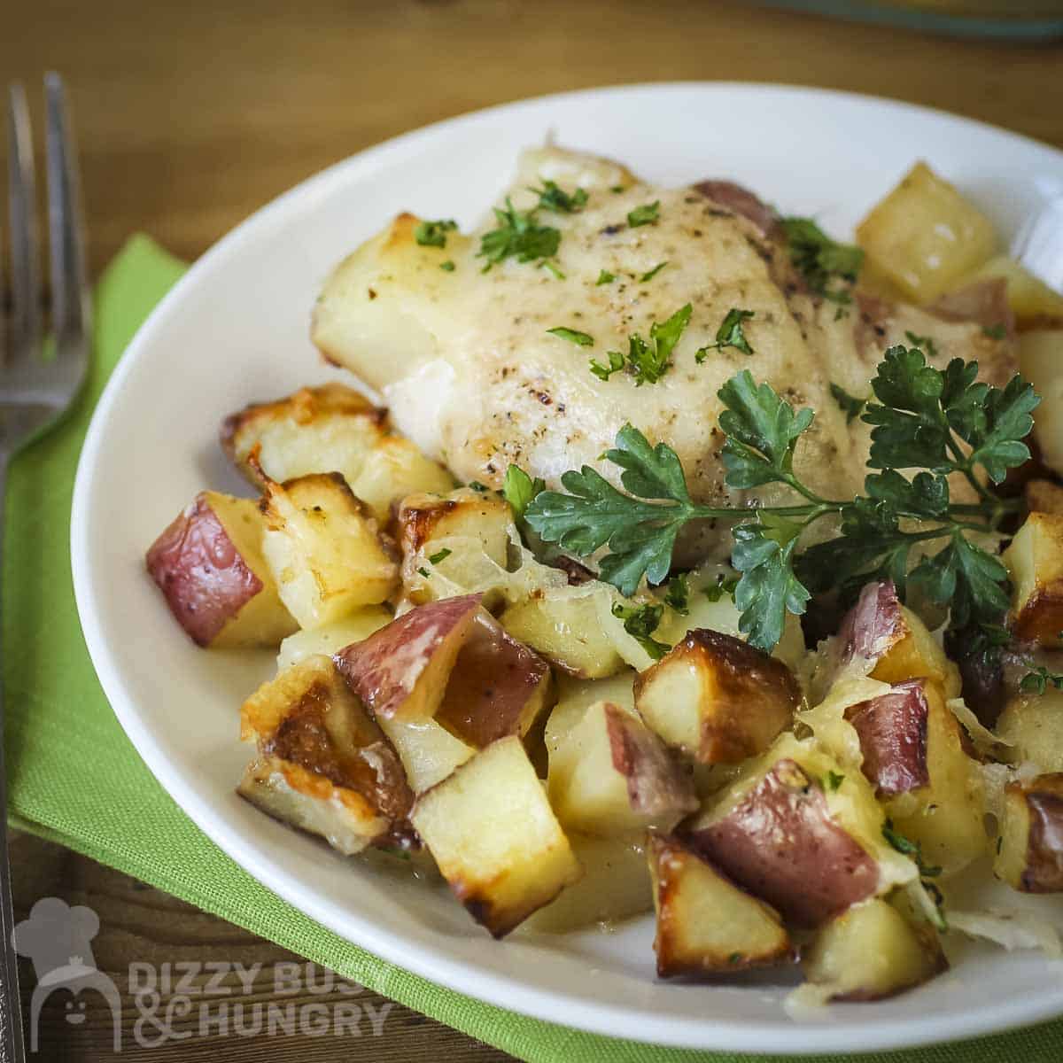 Close up shot of potato chicken bake on a white plate garnished with fresh herbs on a green cloth.