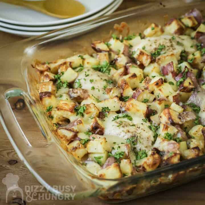 Side shot of chicken potato bake in a casserole dish on a wooden table with plates in the background.