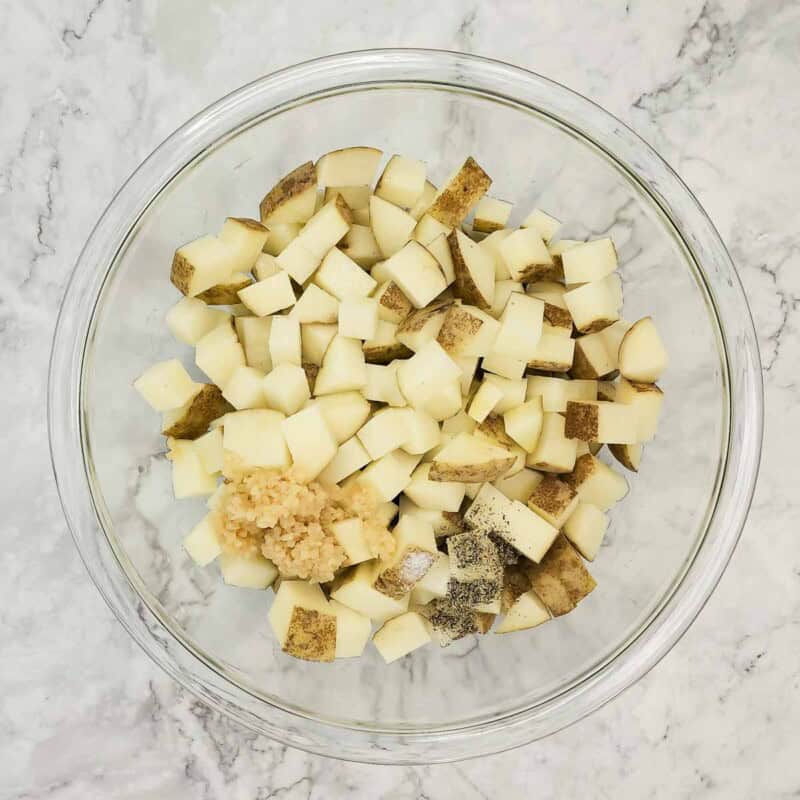 Overhead view of process shot 2 - place the potato cubes in a large bowl and add the garlic, olive oil, salt, and pepper, and toss to coat.