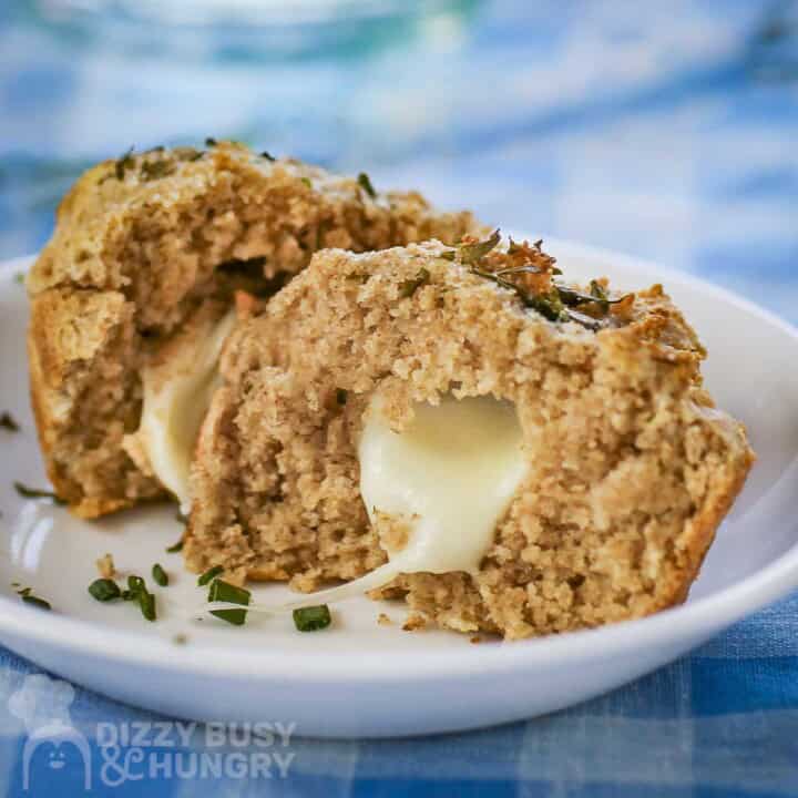 Side shot of a biscuit split in half with mozzarella inside garnished with fresh herbs on a white plate.