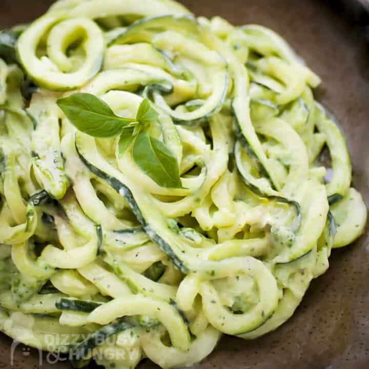 Close up shot of zucchini noodles in avocado sauce garnished with basil in a brown speckled bowl.