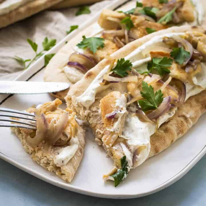 Angled side shot of two chicken pitas on a white plate with a fork taking a piece off of one pita.