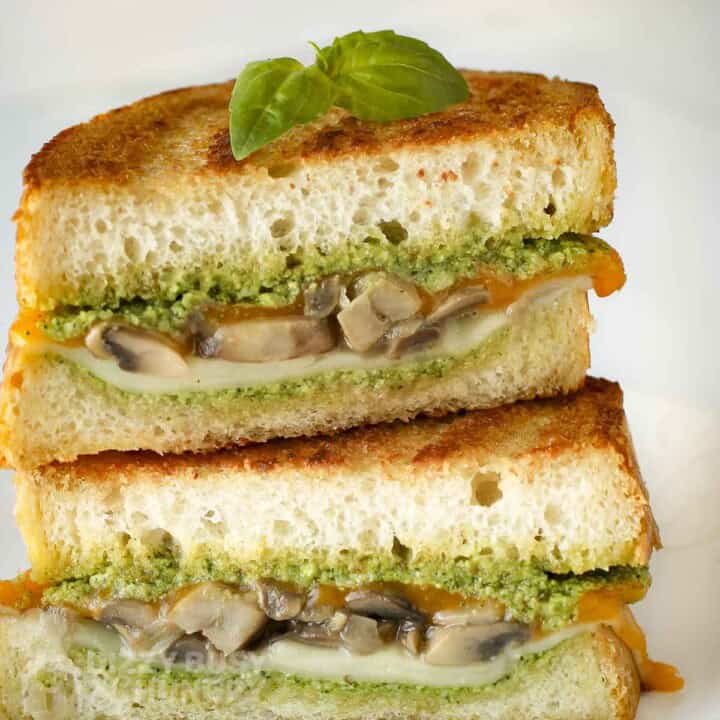 Side shot of two halves of grilled cheese mushroom sandwich garnished with basil with a white background.