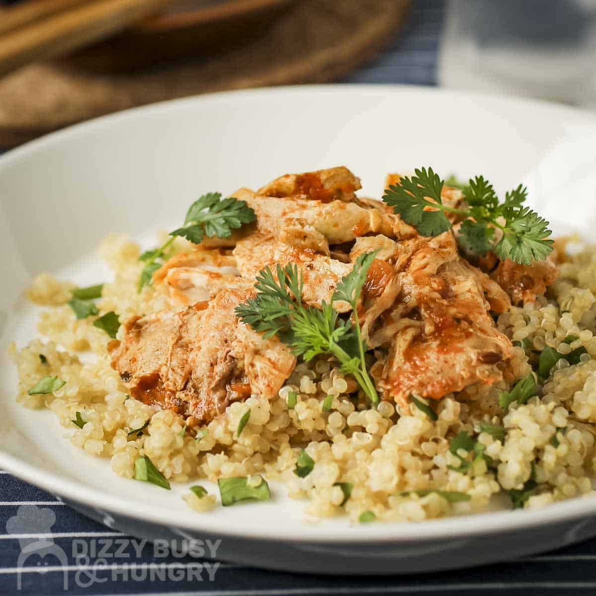 Side view of butter chicken over couscous garnished with fresh herbs on a white bowl.