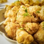 Side shot of cauliflower bites in a tan scalloped bowl garnished with fresh dill.