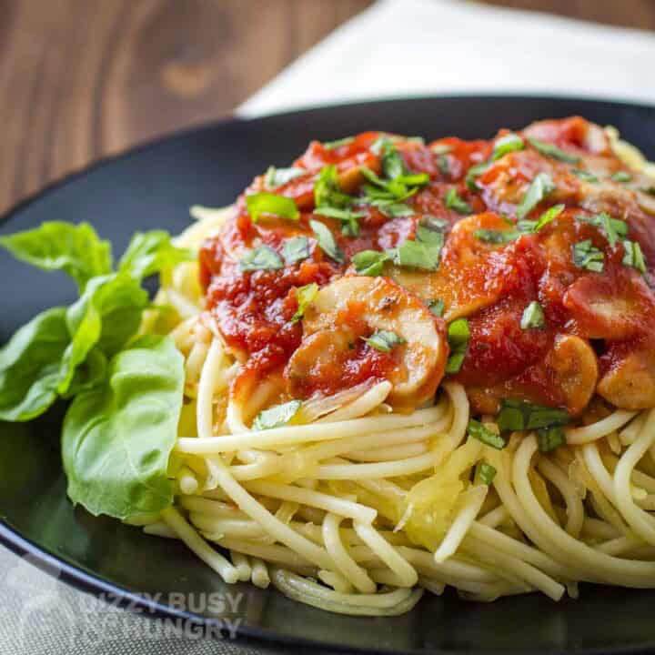 Side shot of pasta with a red mushroom sauce garnished with fresh basil on a black plate.