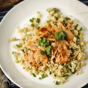 Overhead view of butter chicken over couscous garnished with fresh herbs on a white bowl.