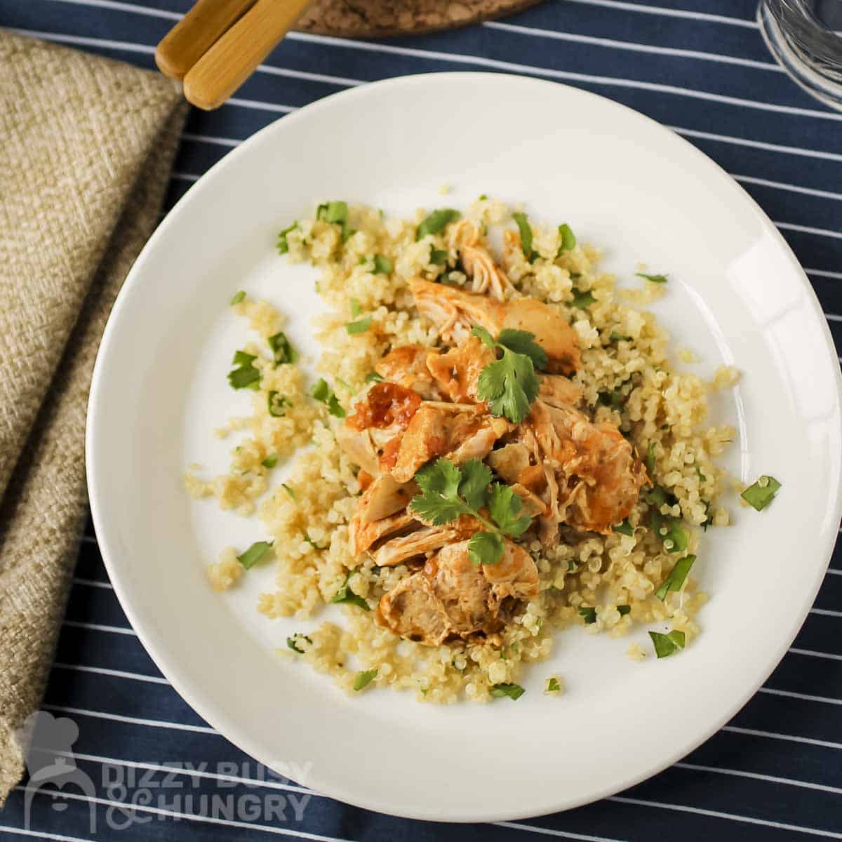 Overhead view of butter chicken over couscous garnished with fresh herbs on a white bowl.