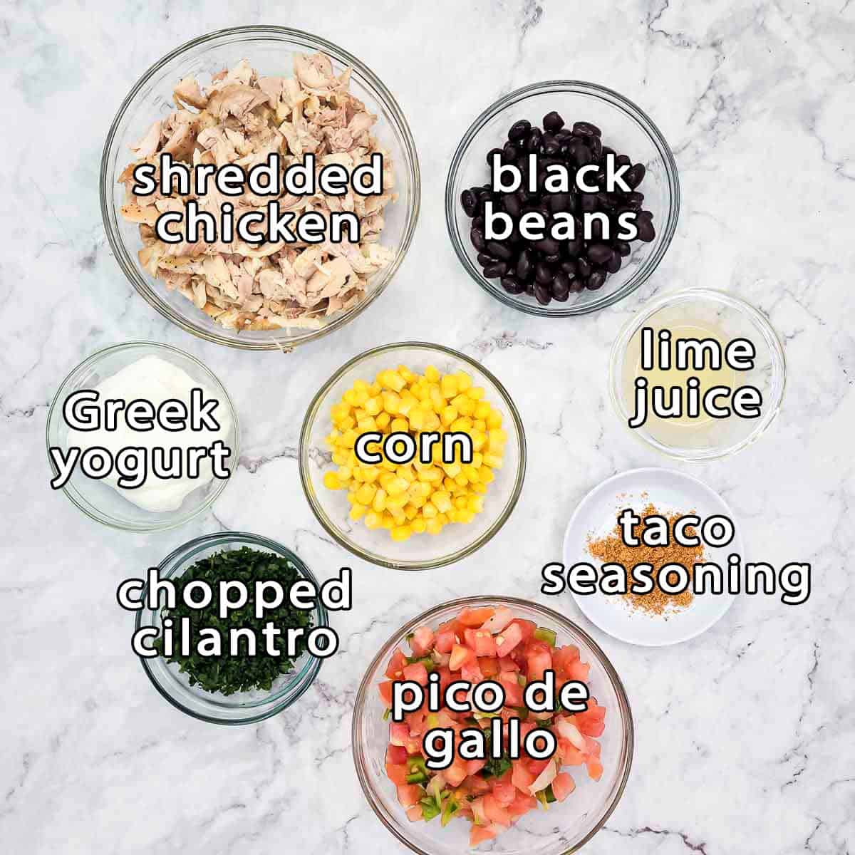 Overhead shot of ingredients - shredded chicken, black beans, greek yogurt, corn, lime juice, chopped cilantro, pico de gallo, and taco seasoning.