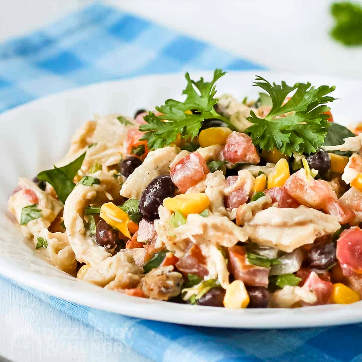 Side shot of southwest chicken salad garnished with fresh cilantro on a white plate with a fork on the side.