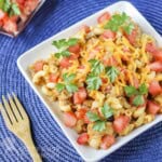 Close up shot of cheeseburger macaroni garnished with fresh cilantro on a white square plate on a blue placemat.