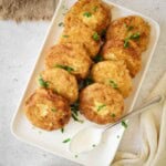 Overhead shot of potato fritters on a white rectangle plate garnished with fresh parsley.