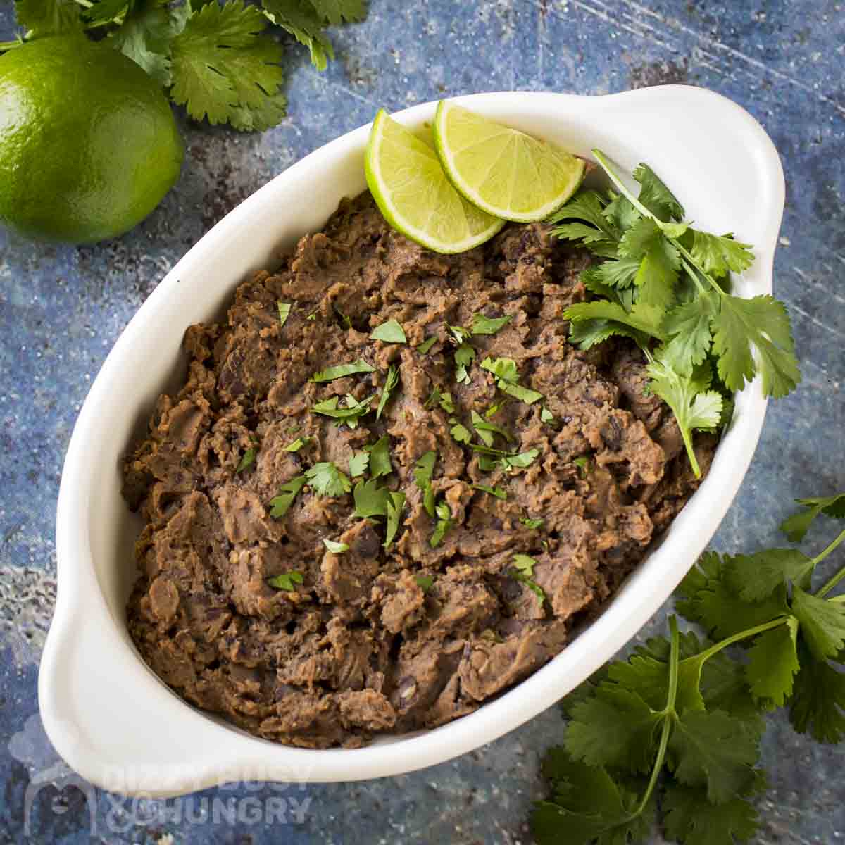Side shot of refried black beans in a small white baking dish garnished with fresh parsley and lime.