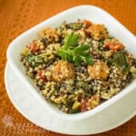 Side shot of chorizo and quinoa in a white bowl on a white plate on an orange cloth.