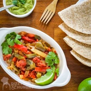 Overhead shot of veggie fajitas in a white dish garnished with cilantro with tortillas and guacamole on the side.