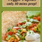 Close up shot of veggie fajitas in a tortilla garnished with cilantro and sour cream with a lime wedge on the side.