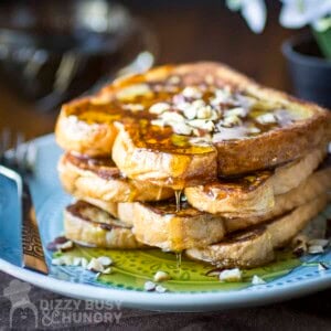 Side view of a stack of french toast with syrup and chopped almonds on a blue plate with a fork on the side.