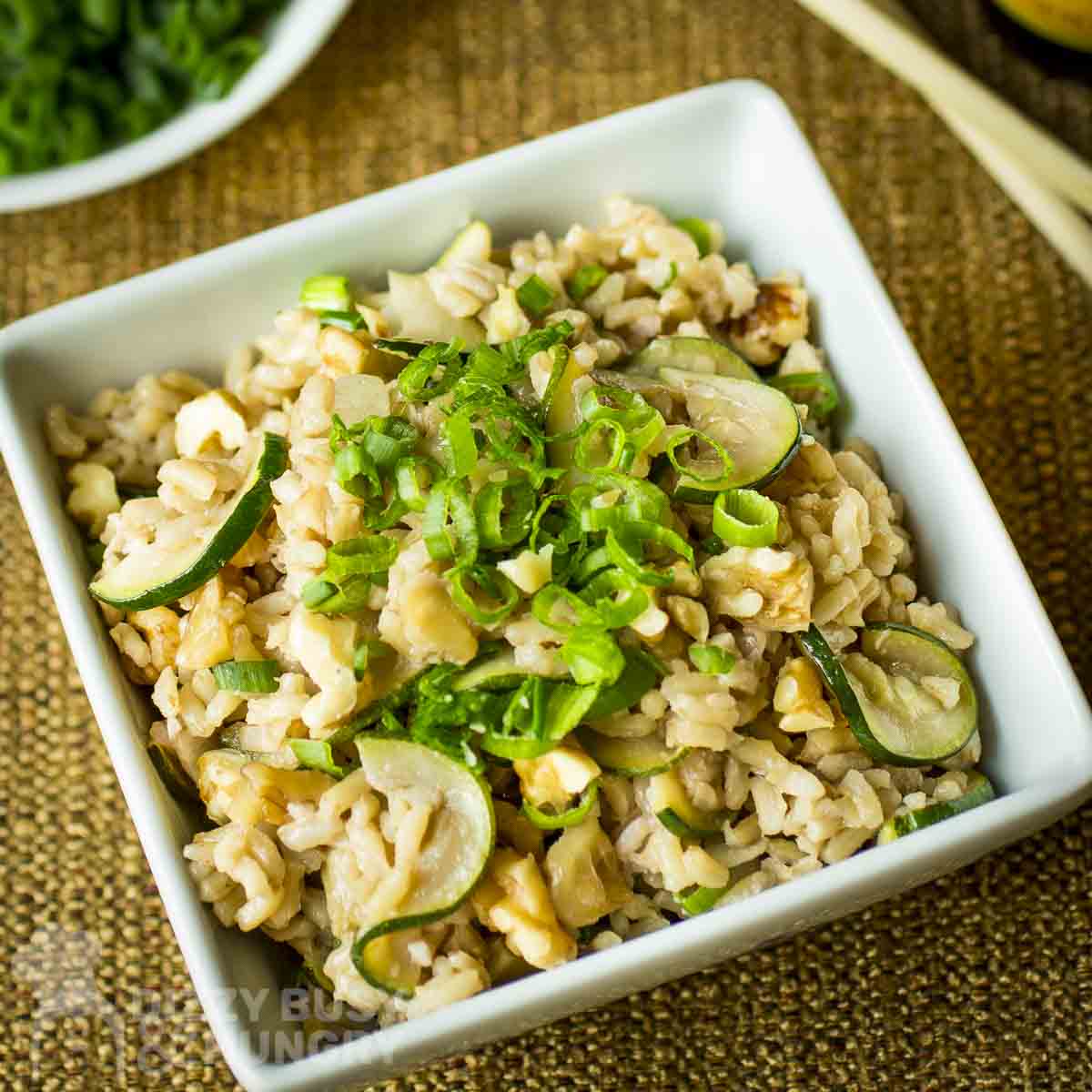 Overhead shot of a square white bowl with zucchini fried rice garnished with green onions on a burlap cloth.