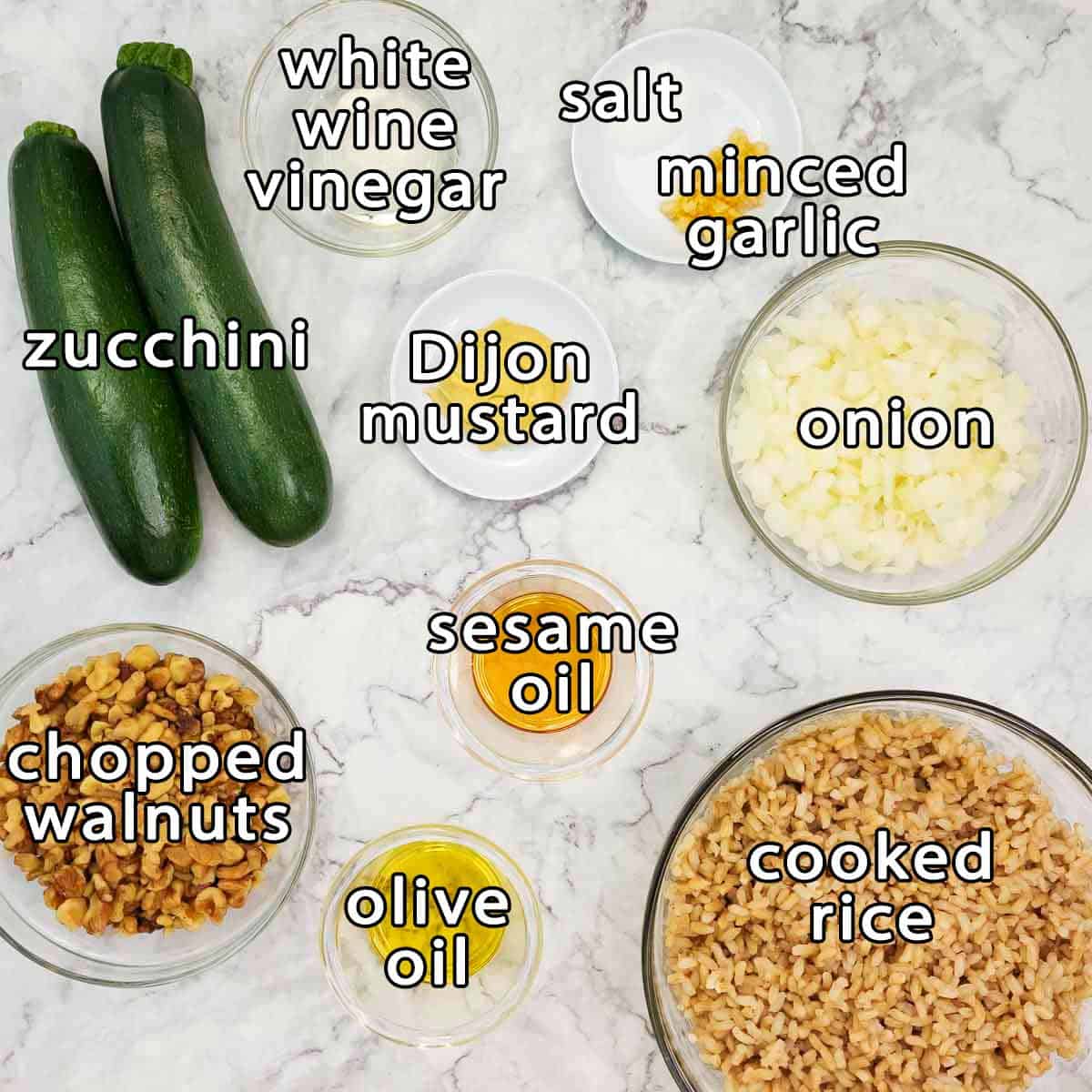 Overhead shot of ingredients - zucchini, white wine vinegar, salt, minced garlic, dijon mustard, onion, sesame oil, chopped walnuts, olive oil, and cooked rice.