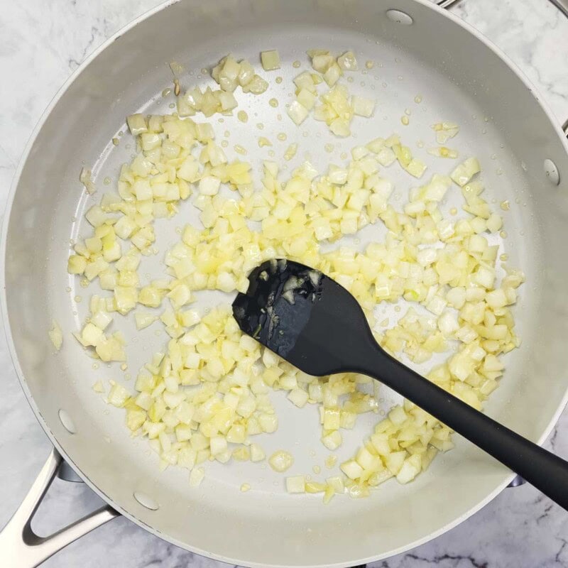 Overhead view of process shot 2 - in a large skillet, heat the sesame or vegetable oil over medium high heat. Add the onion and garlic and saute for about 2-3 minutes.