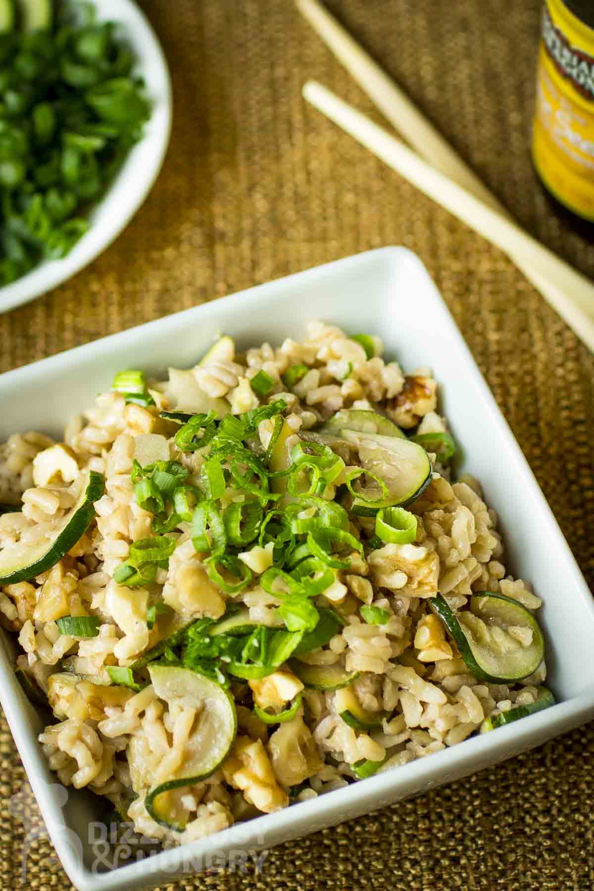 Overhead shot of a square white bowl with zucchini fried rice garnished with green onions on a burlap cloth.