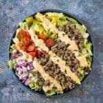 Overhead shot of big mac bowl drizzled with sauce and garnished with herbs in a blue bowl.