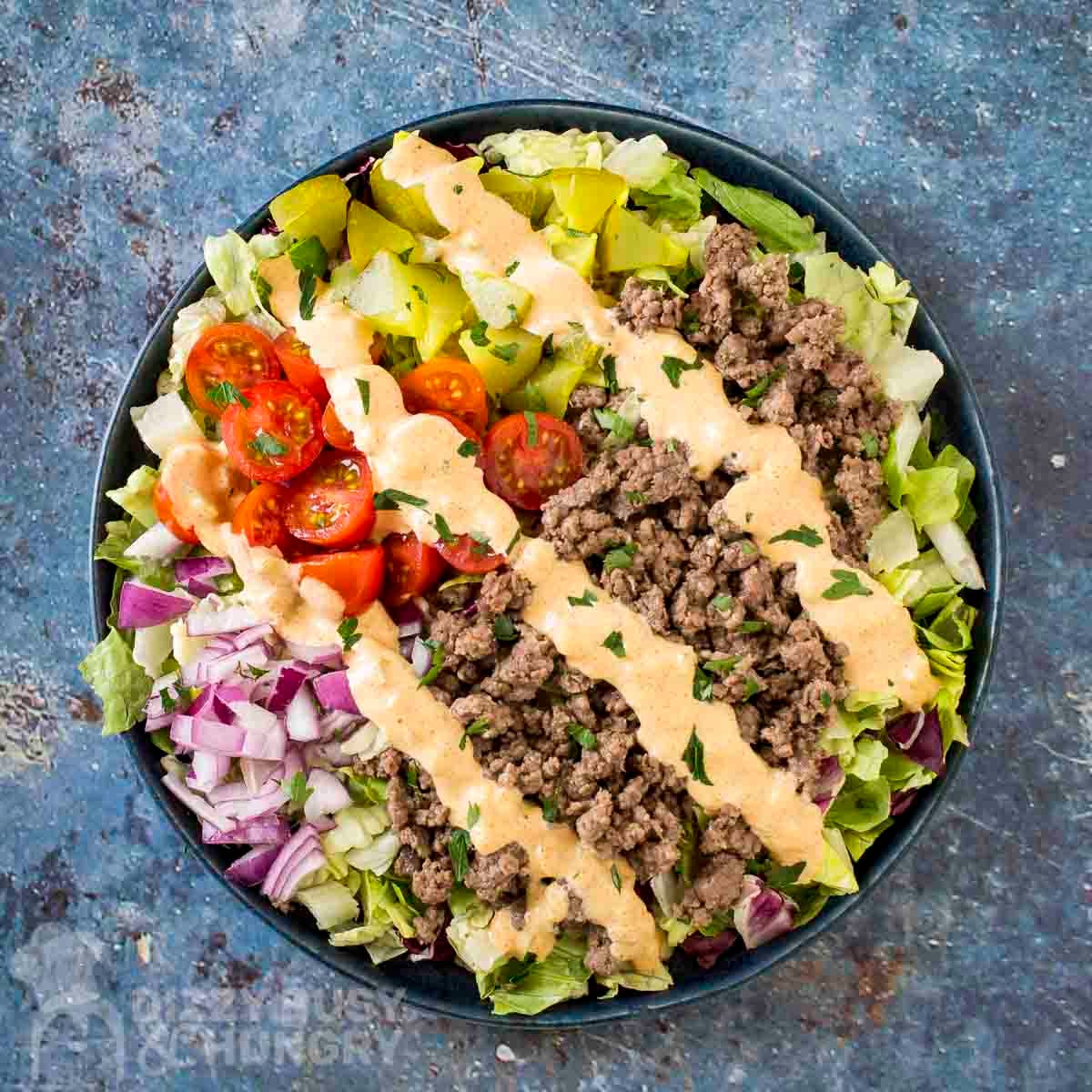 Overhead shot of big mac bowl drizzled with sauce and garnished with herbs in a blue bowl.