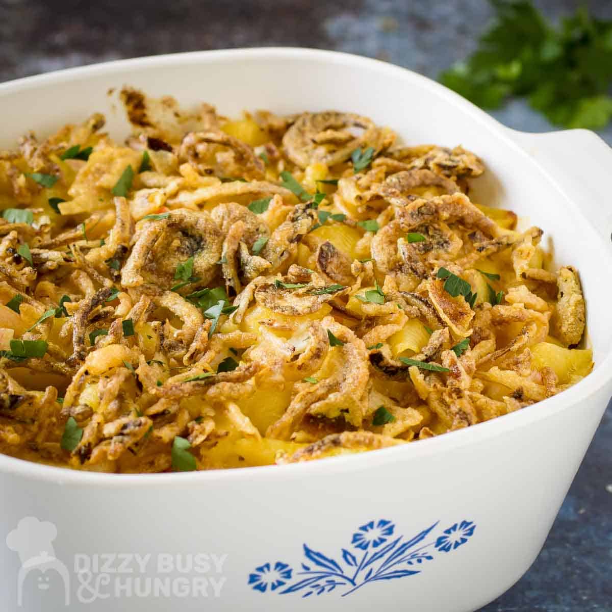 Side shot of seafood mac and cheese garnished with french fried onions and fresh herbs in a white baking dish.
