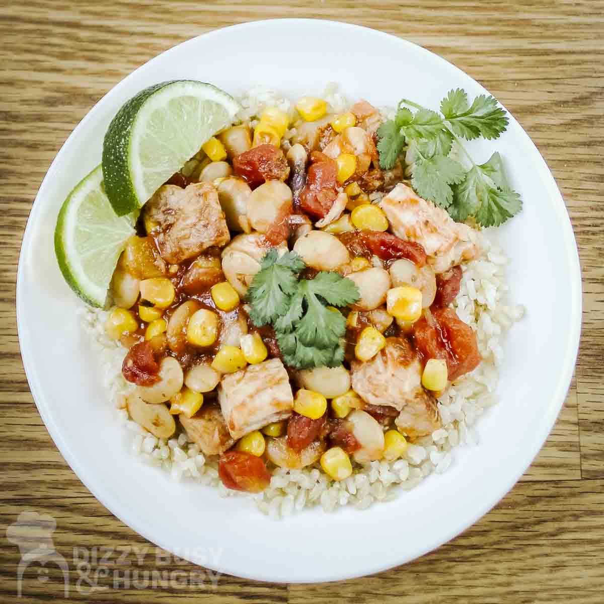 Overhead shot of mango salsa chicken and butter beans over rice garnished with fresh herbs and lime slices in a white bowl.